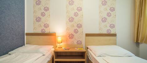 A room with two beds, a nightstand with a lamp, and floral wallpaper.