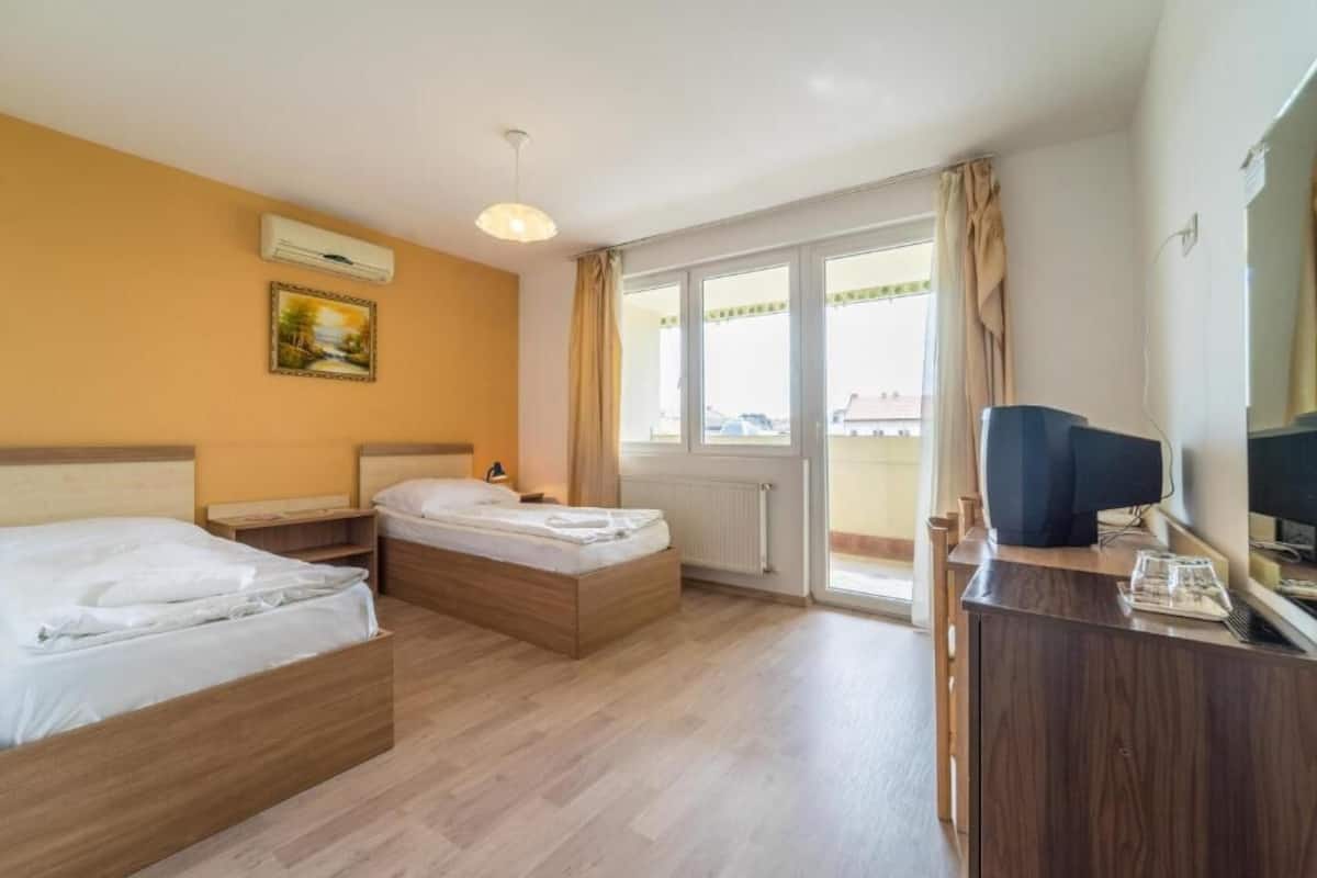 Ein Hotelzimmer mit zwei Betten, einem Schreibtisch, einem Fernseher und einem Fenster mit Vorhängen.