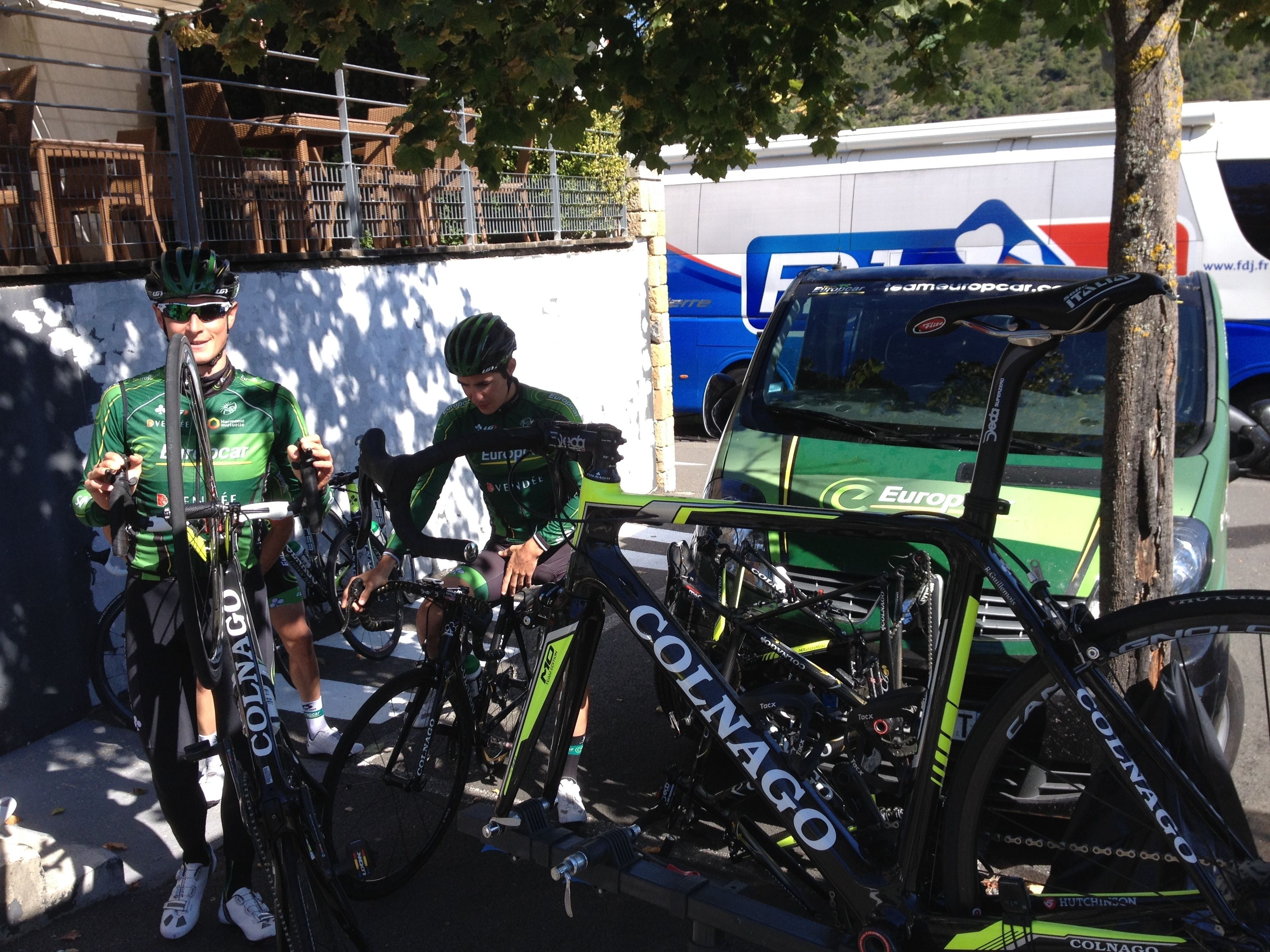 Un ciclista con una maglia verde seduto sulla bicicletta accanto a un veicolo parcheggiato con un logo ben visibile.