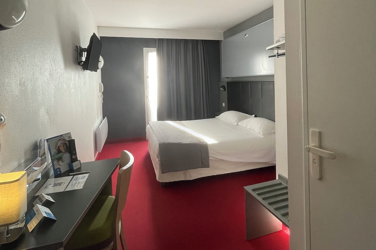 A hotel room with a bed, a desk with a chair, a TV, and a door.