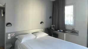 A hotel room with a single bed, a desk with a chair, a window with curtains, a coat rack, and a ceiling light. - Brit Hotel Confort Marvejols (Marvejols)