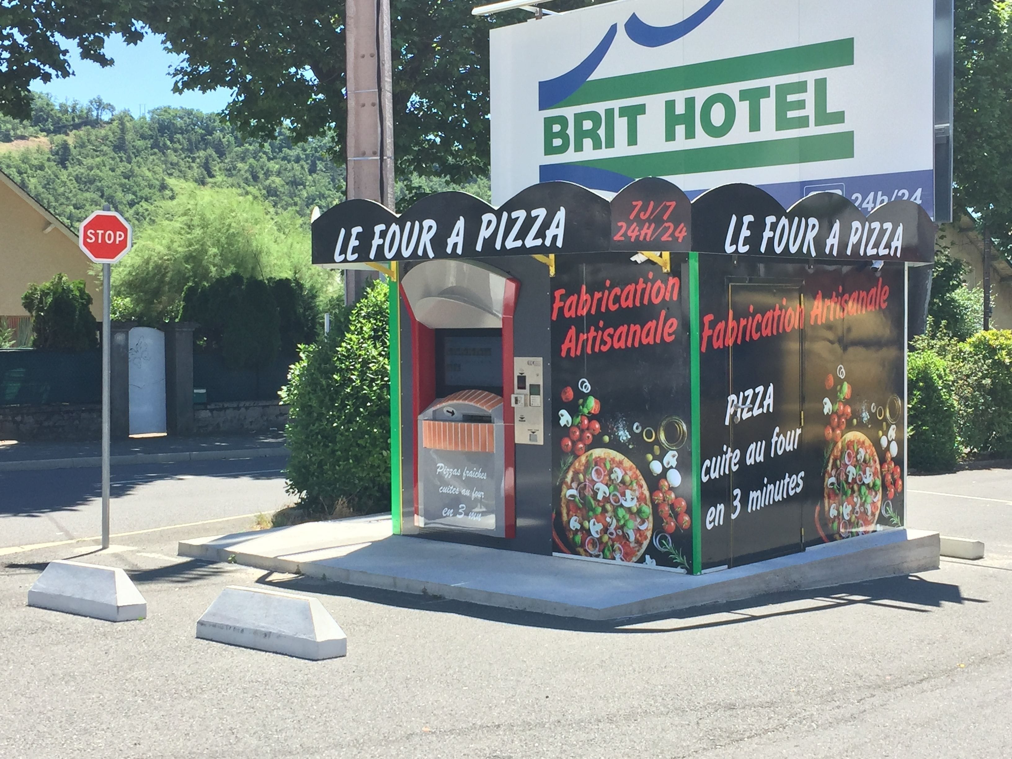 A roadside sign for a pizza restaurant with a stop sign nearby.