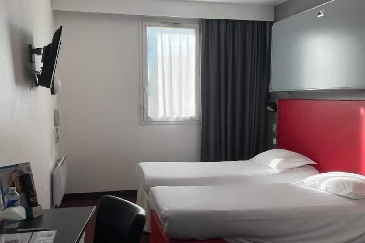 A hotel room with two beds, a desk, a chair, a TV, and a window with curtains.