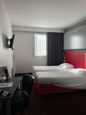 A hotel room with two beds, a desk, a chair, a TV, and a window with curtains. - Brit Hotel Confort Marvejols (Marvejols)