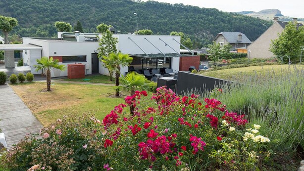 A modern house with a flat roof, a patio area, and a garden with flowering plants. - Brit Hotel Confort Marvejols (Marvejols)