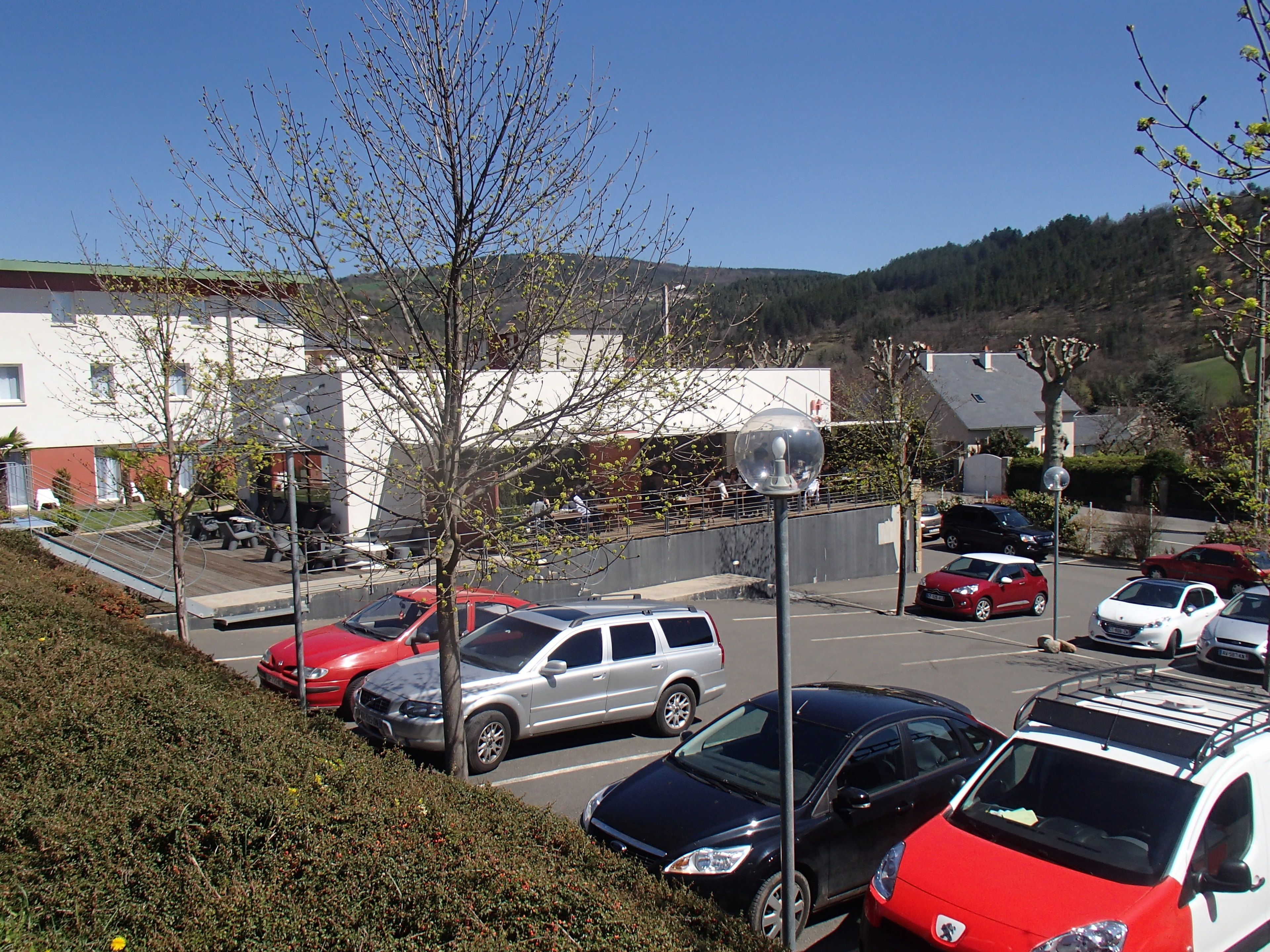 Un parcheggio con diverse auto, un edificio con tetto verde e una collina sullo sfondo.