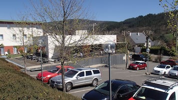 Un parcheggio con diverse auto, un edificio con tetto verde e una collina sullo sfondo.