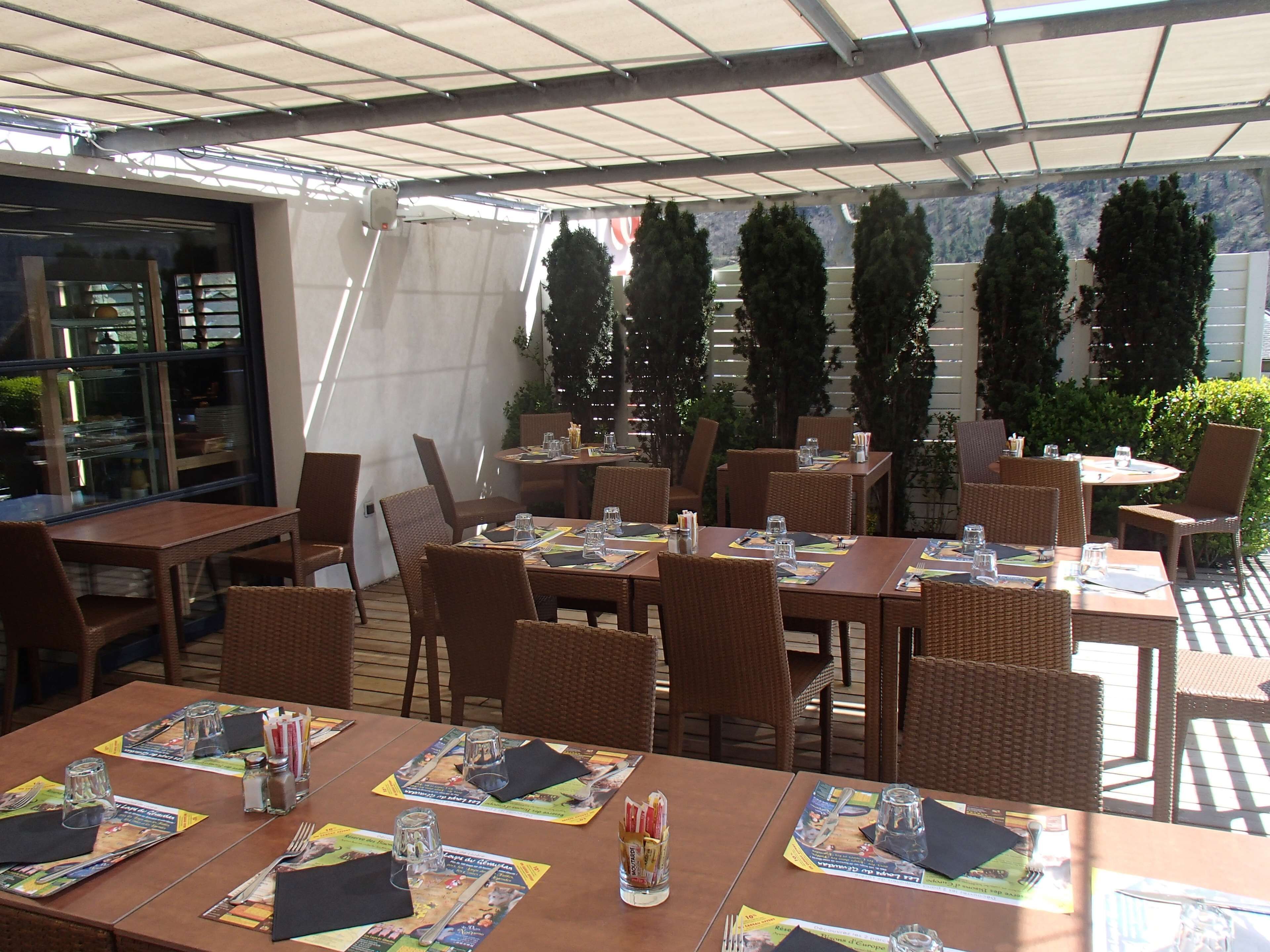 Un área de comedor al aire libre con mesas dispuestas para dos, con sillas de mimbre y menús.