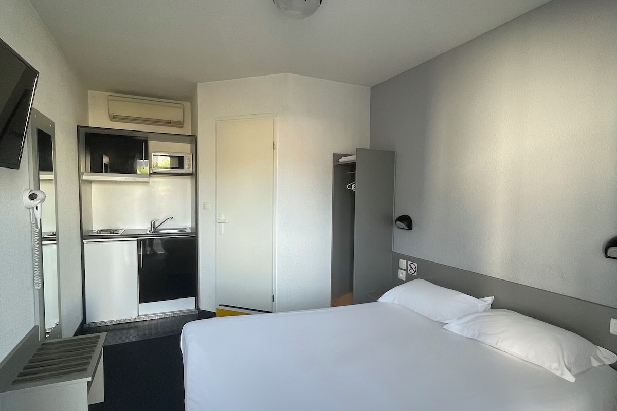 A hotel room with a bed, a desk, a microwave, a mini-fridge, and a small kitchenette.