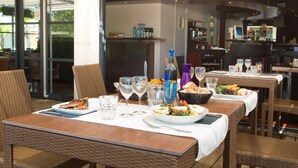 An outdoor dining area with wicker furniture, glassware, and a variety of dishes. - Brit Hotel Confort Marvejols (Marvejols)
