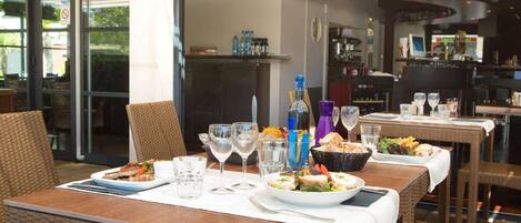 Un comedor al aire libre con mobiliario de mimbre, cristalería y una variedad de platos.