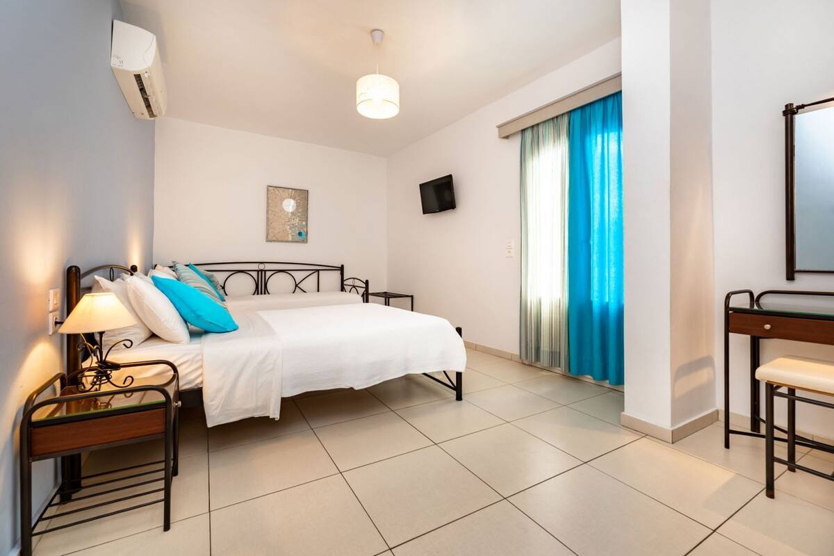 Habitació d'hotel amb llit, taulell de nit, làmpada, aire condicionat i televisió.