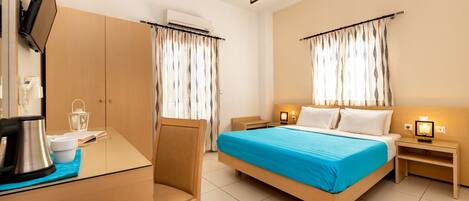 Habitación de hotel con cama, escritorio, silla, televisor y mesita de noche con lámpara.