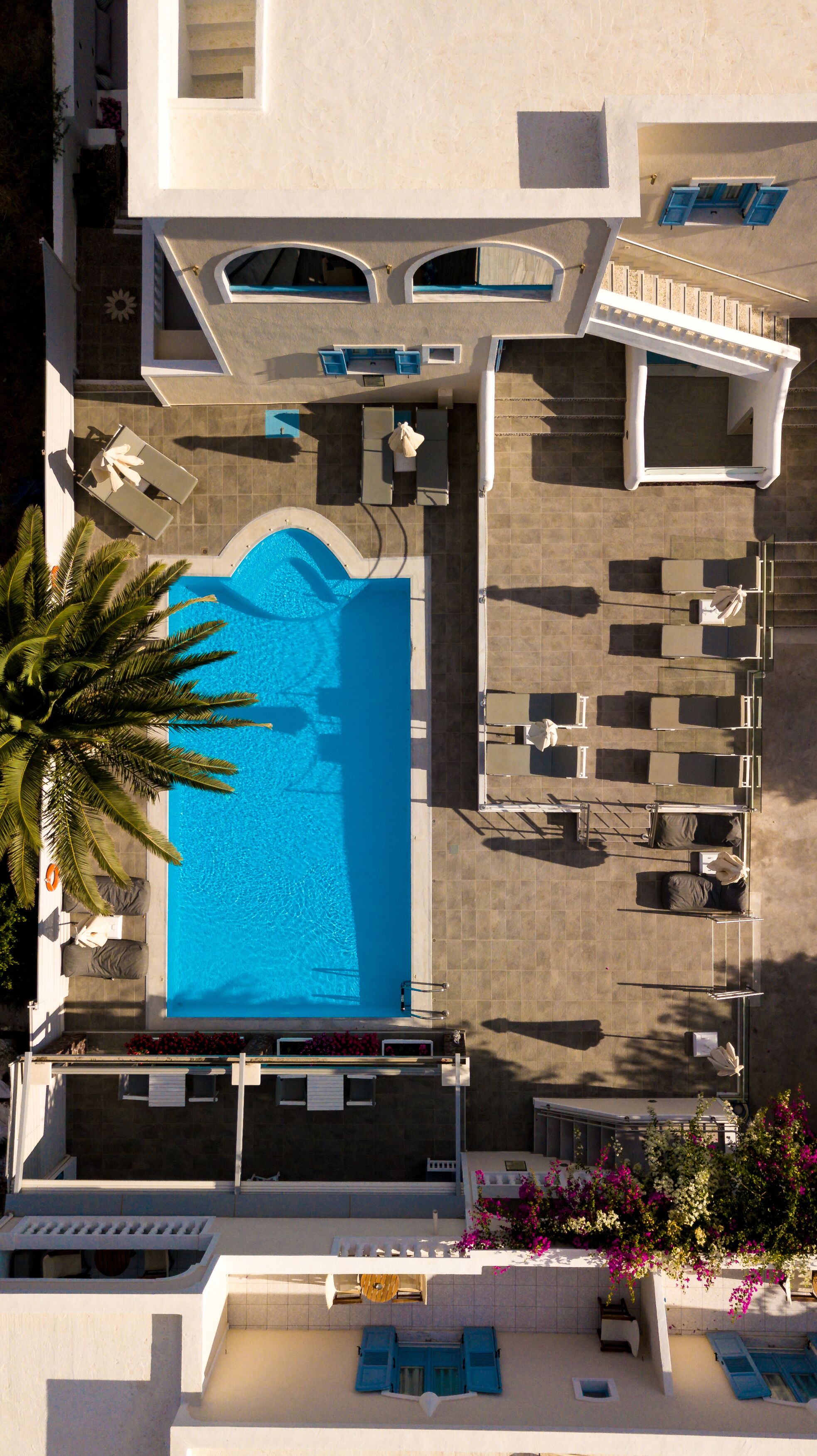 An aerial view of a hotel with a swimming pool, sun loungers, and a covered seating area.