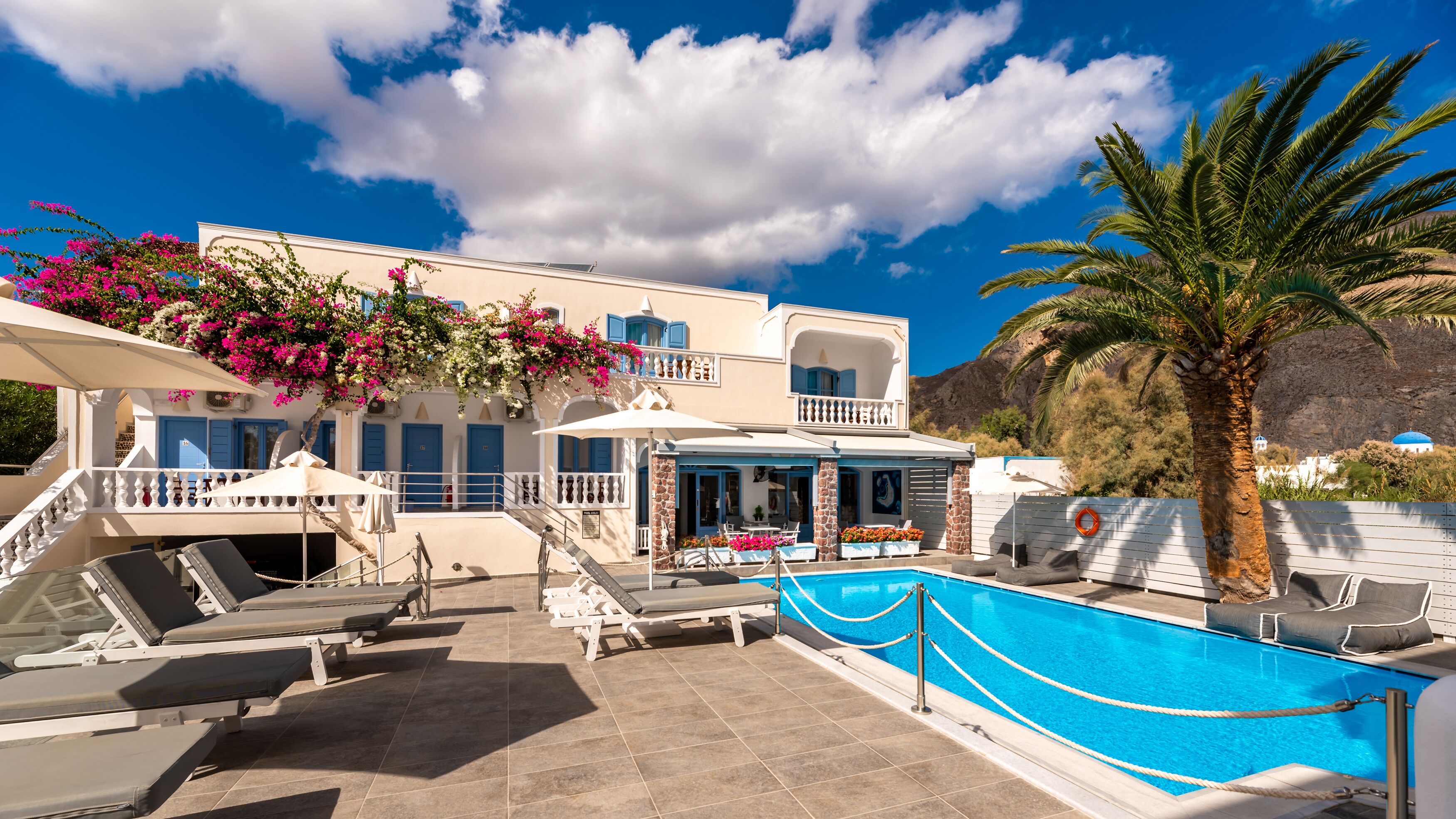 Un resort con piscina, camas sol y montañas al fondo.