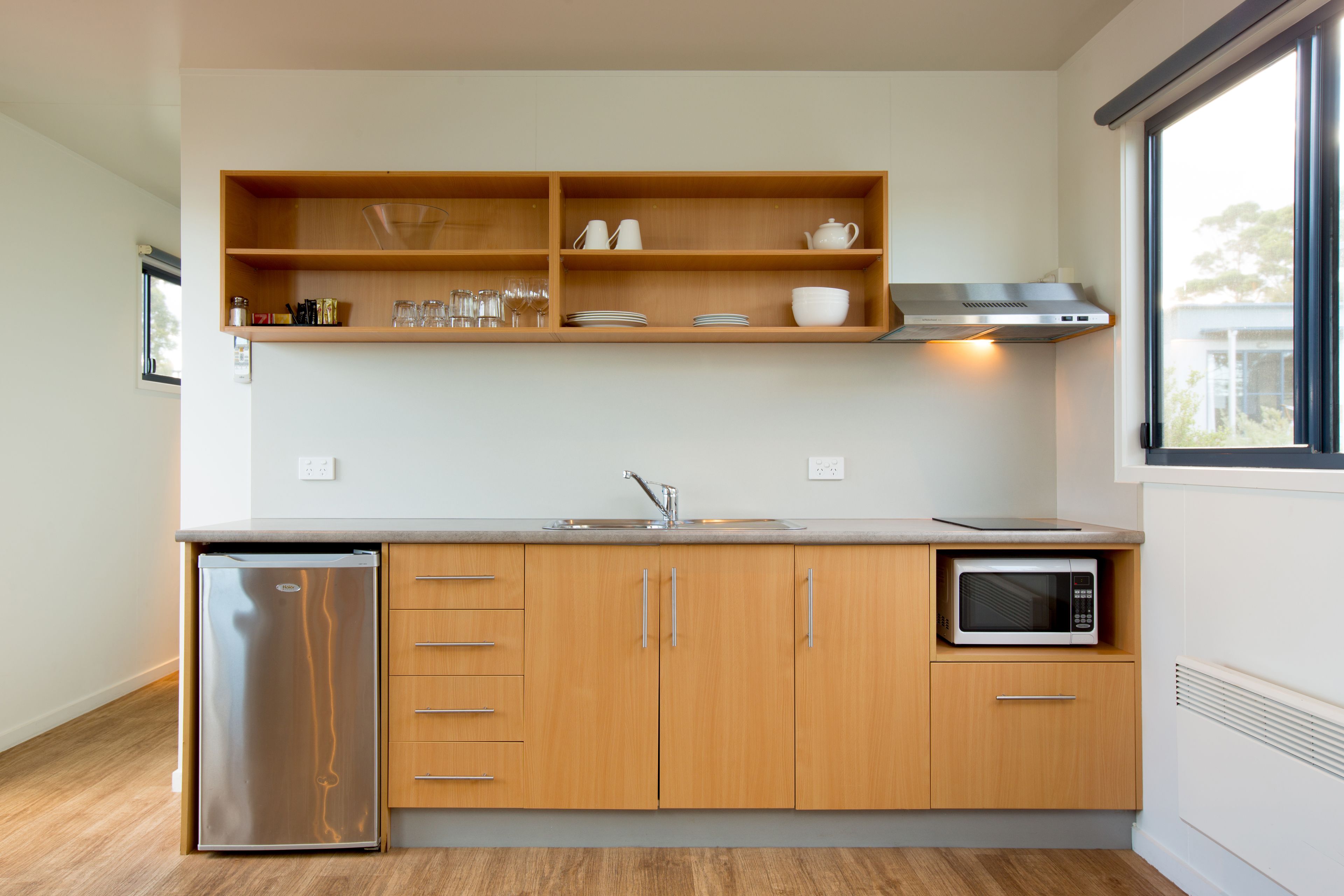 A modern kitchen with wooden cabinets, a stainless steel refrigerator, a microwave, and a built-in oven.