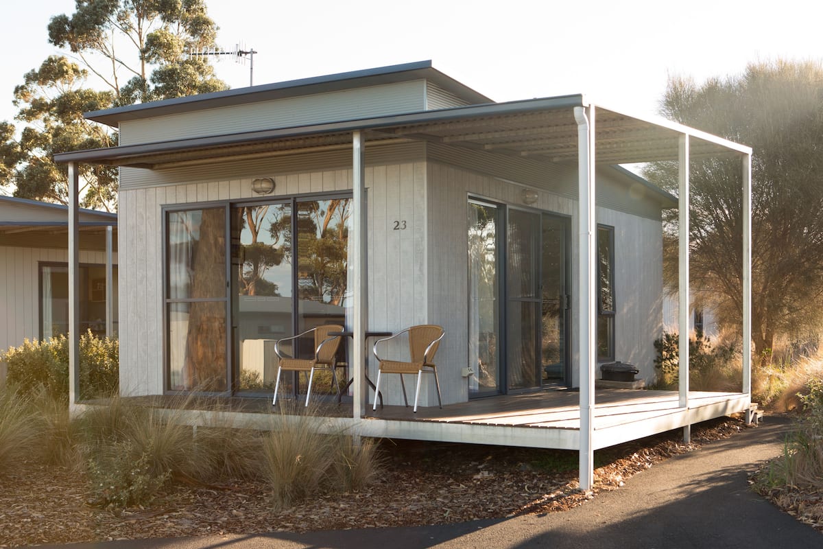 Een modern huis met een overdekte veranda, twee stoelen en het nummer 23 op de deur.