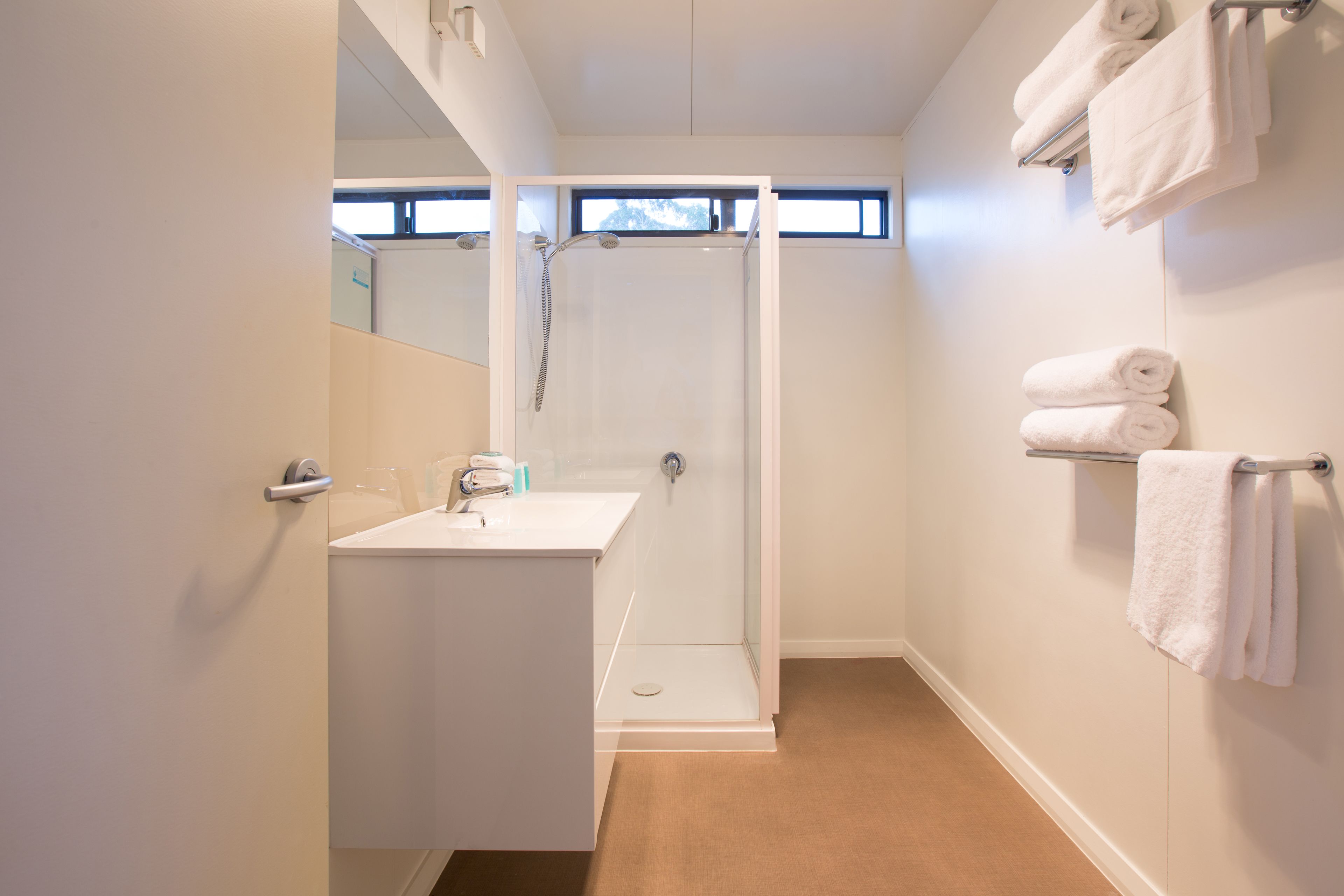 Un baño moderno con ducha de vidrio, lavamanos blanco y toallero.