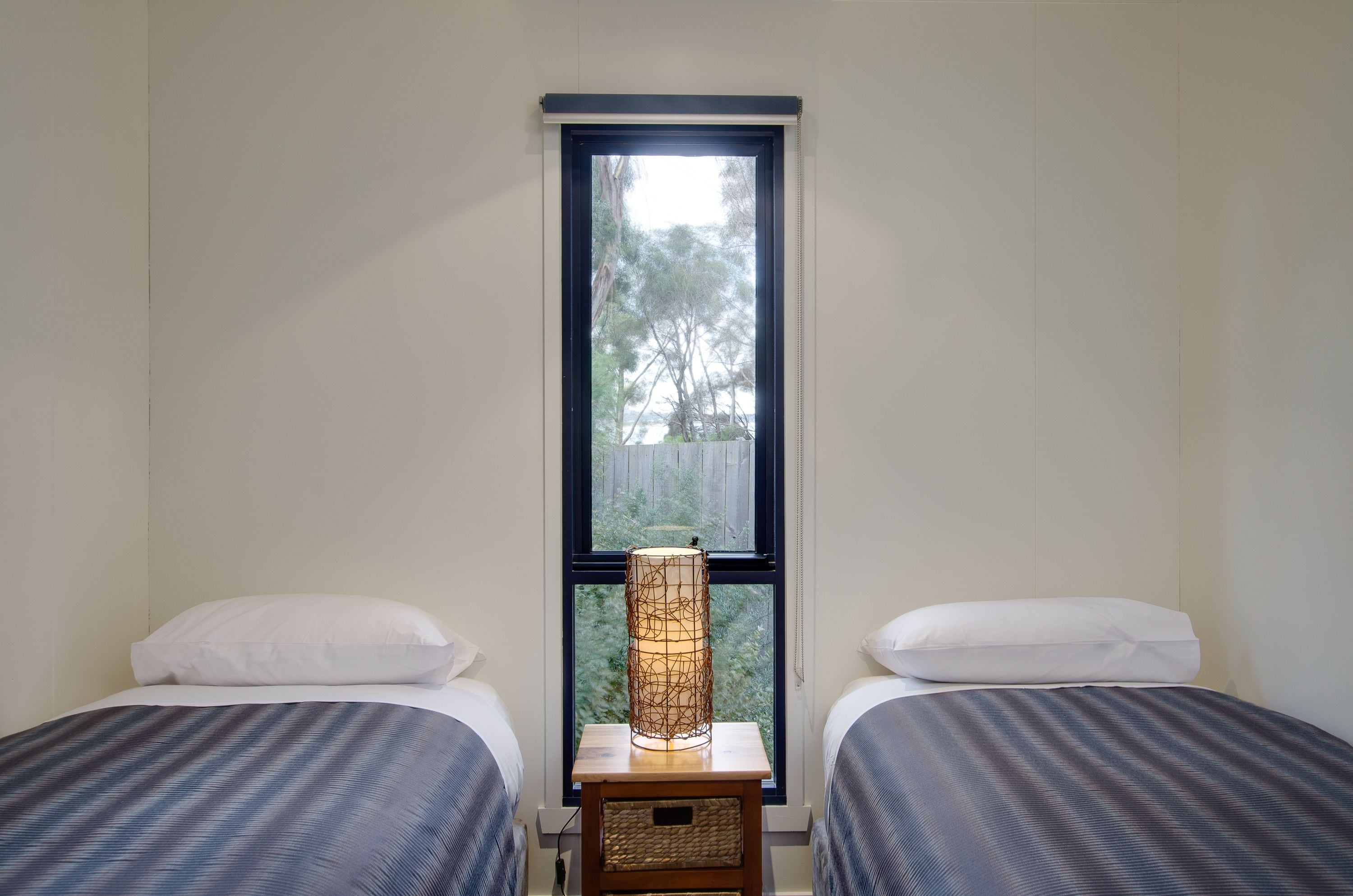 A bedroom with two beds, a nightstand, a lamp, and a window with a view of trees.