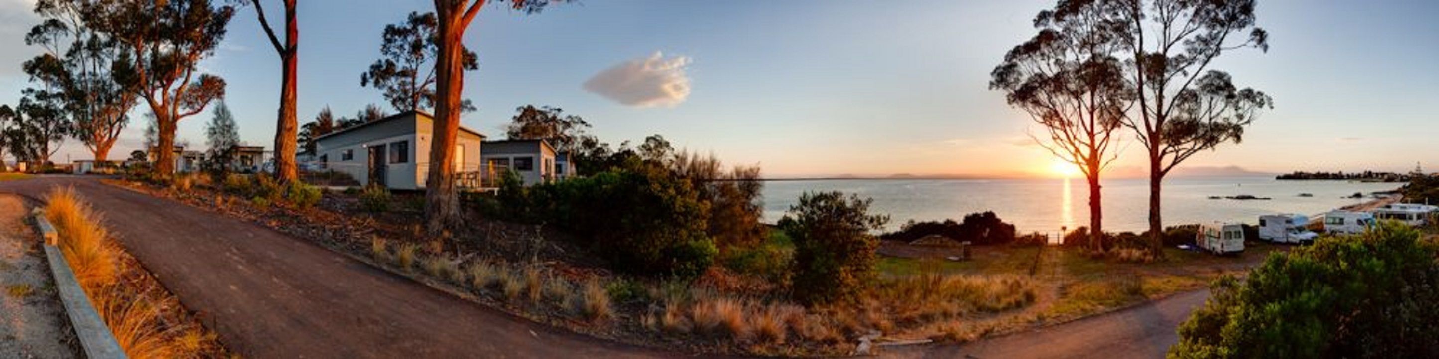 A coastal road with a house and RVs parked nearby.