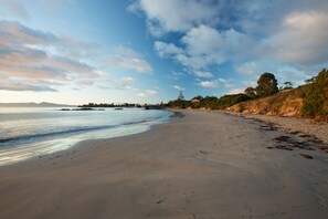 A wide sandy beach with gentle waves, a clear sky, and distant trees. - Swansea Beach Chalets (Swansea)