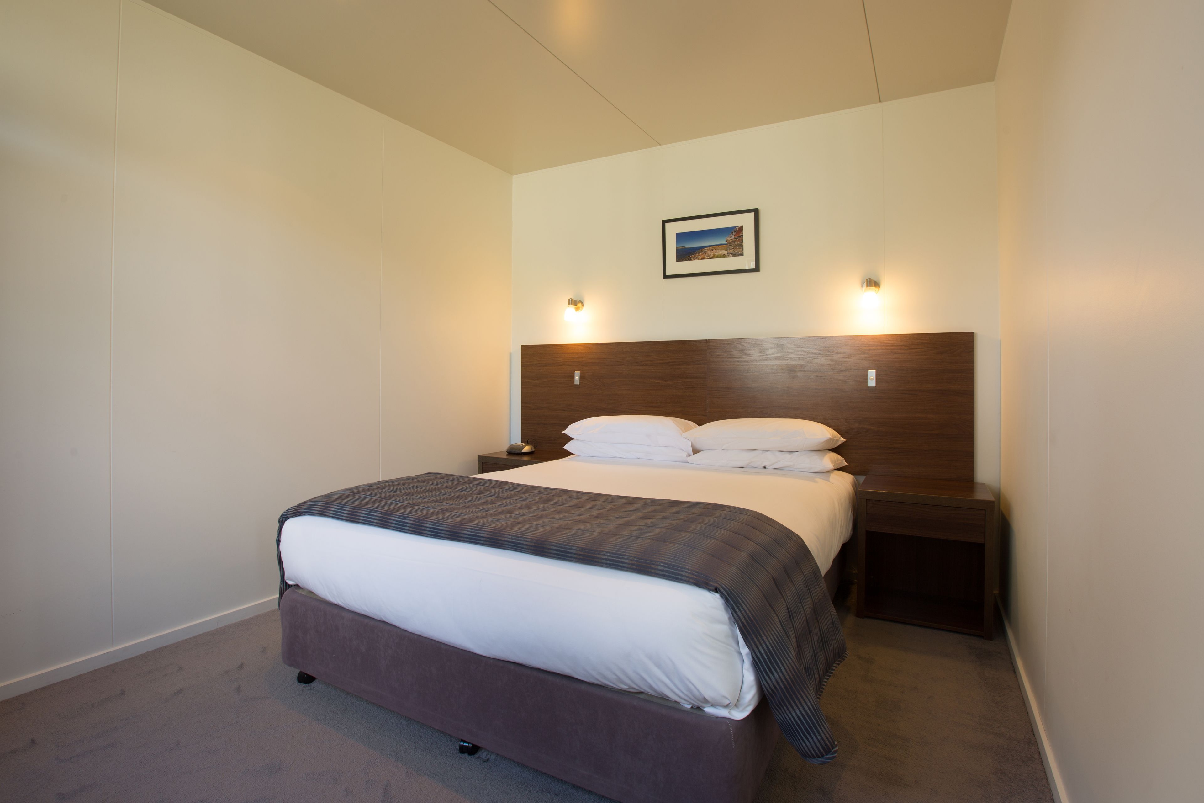 A neatly made bed with a wooden headboard, two bedside tables with lamps, and a framed picture on the wall.