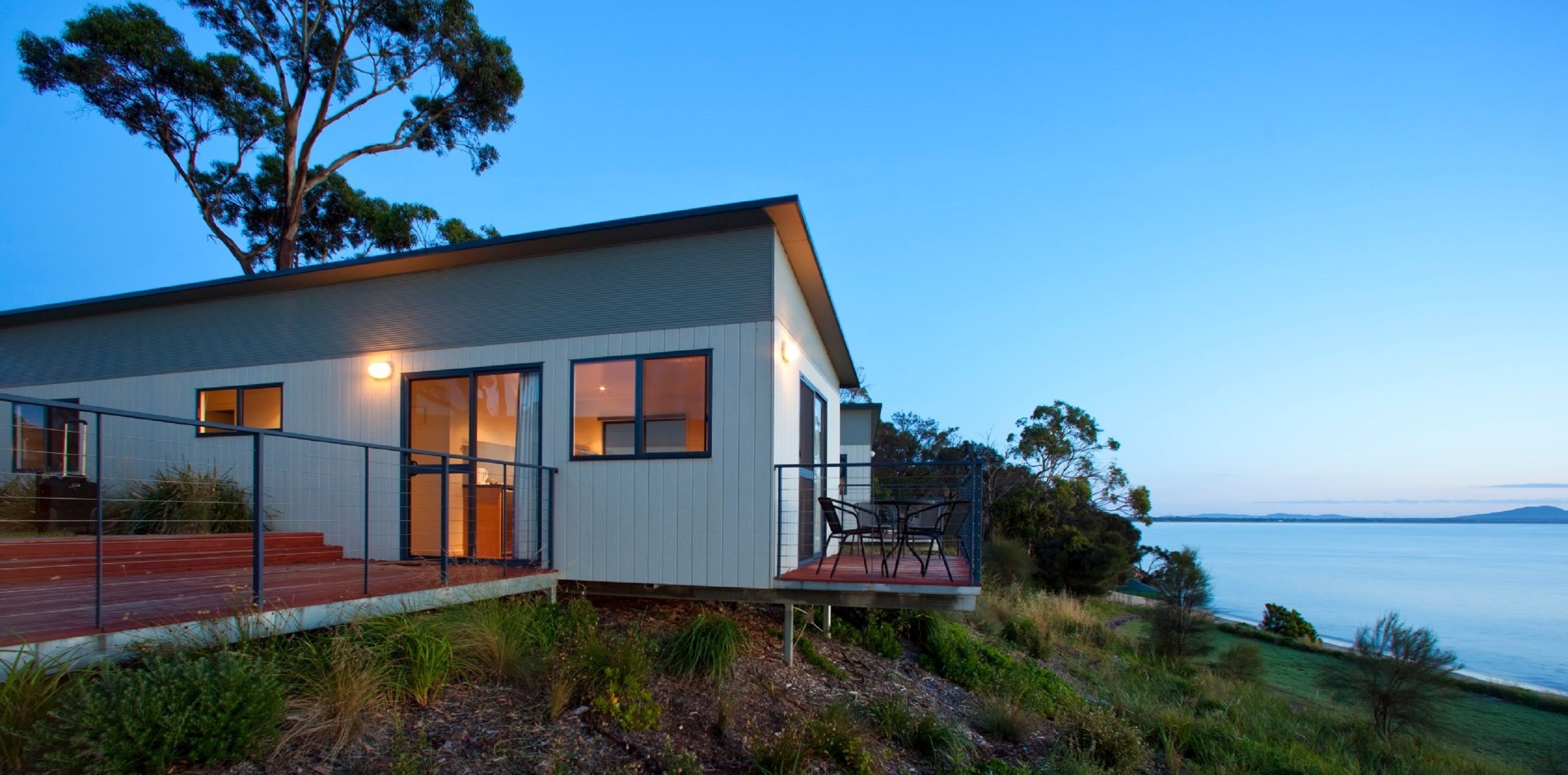 A modern house with large windows, a deck, and a view of the sea.