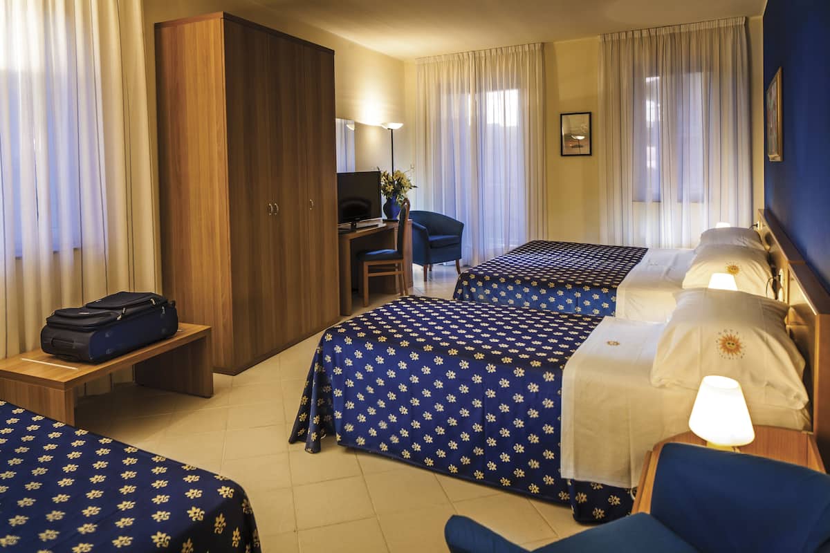Habitación de hotel con dos camas, un escritorio, una silla, un armario y un televisor.