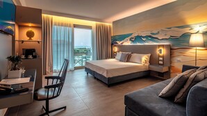 A modern hotel room with a bed, a desk, a chair, a sofa, and a balcony with a view. - Riviera del Sole (Piraino)