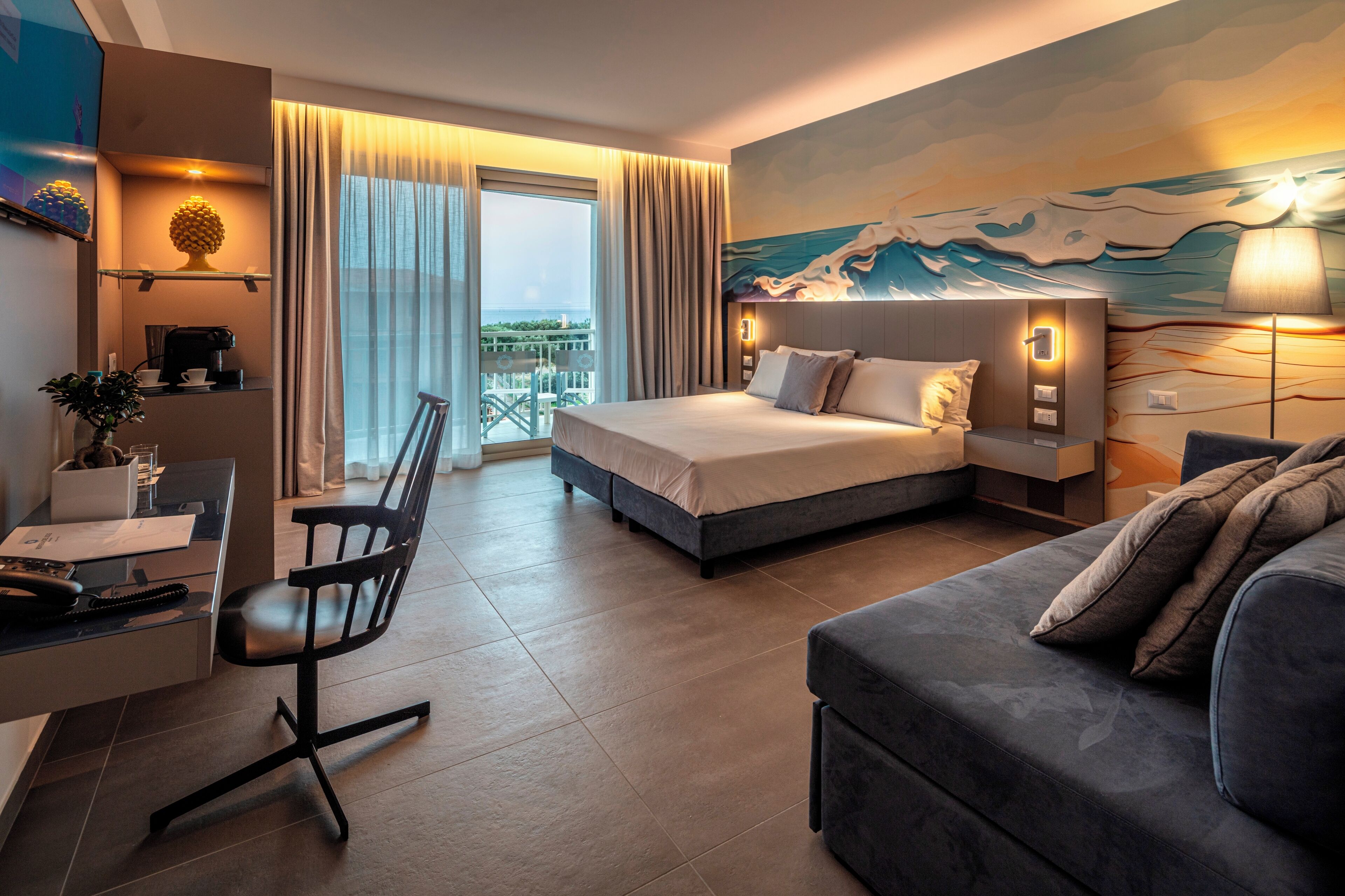 Una habitación de hotel moderna con cama, escritorio, sillón, sofá y balcón con vistas.