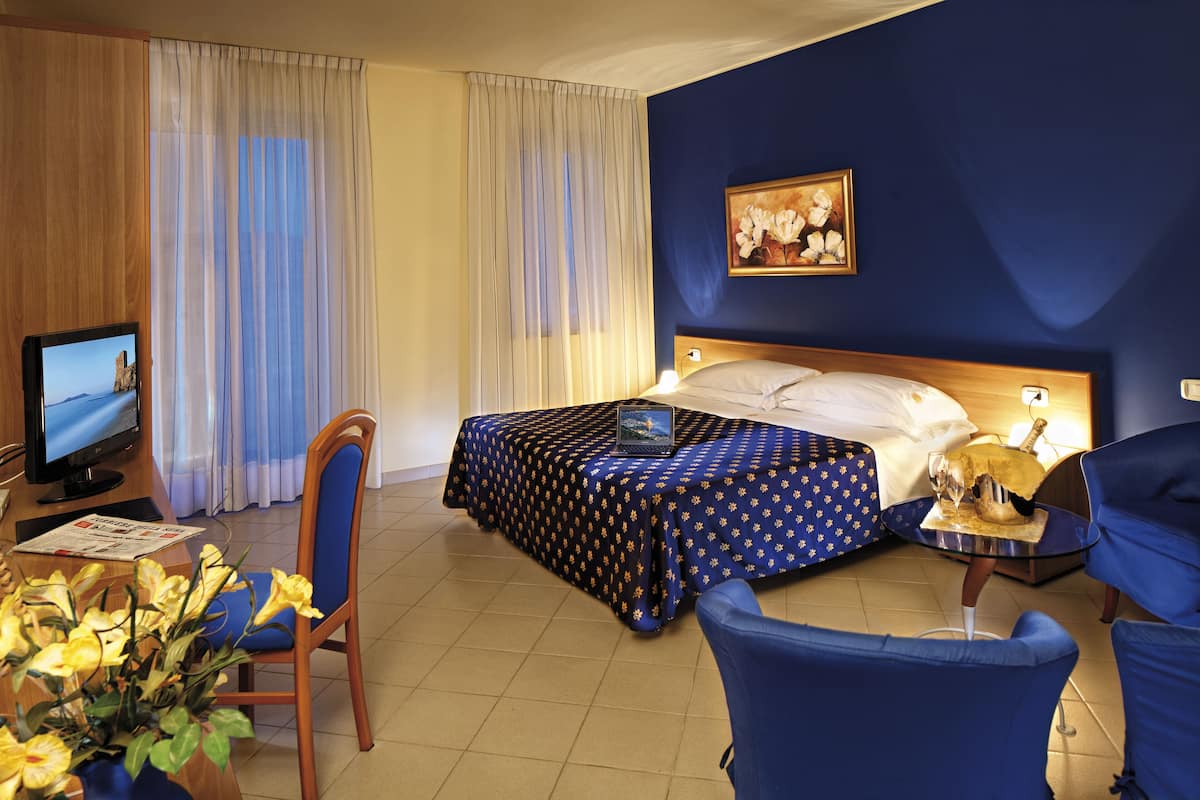Una habitación de hotel con cama, escritorio con computadora, silla, televisor y un cuadro en la pared.