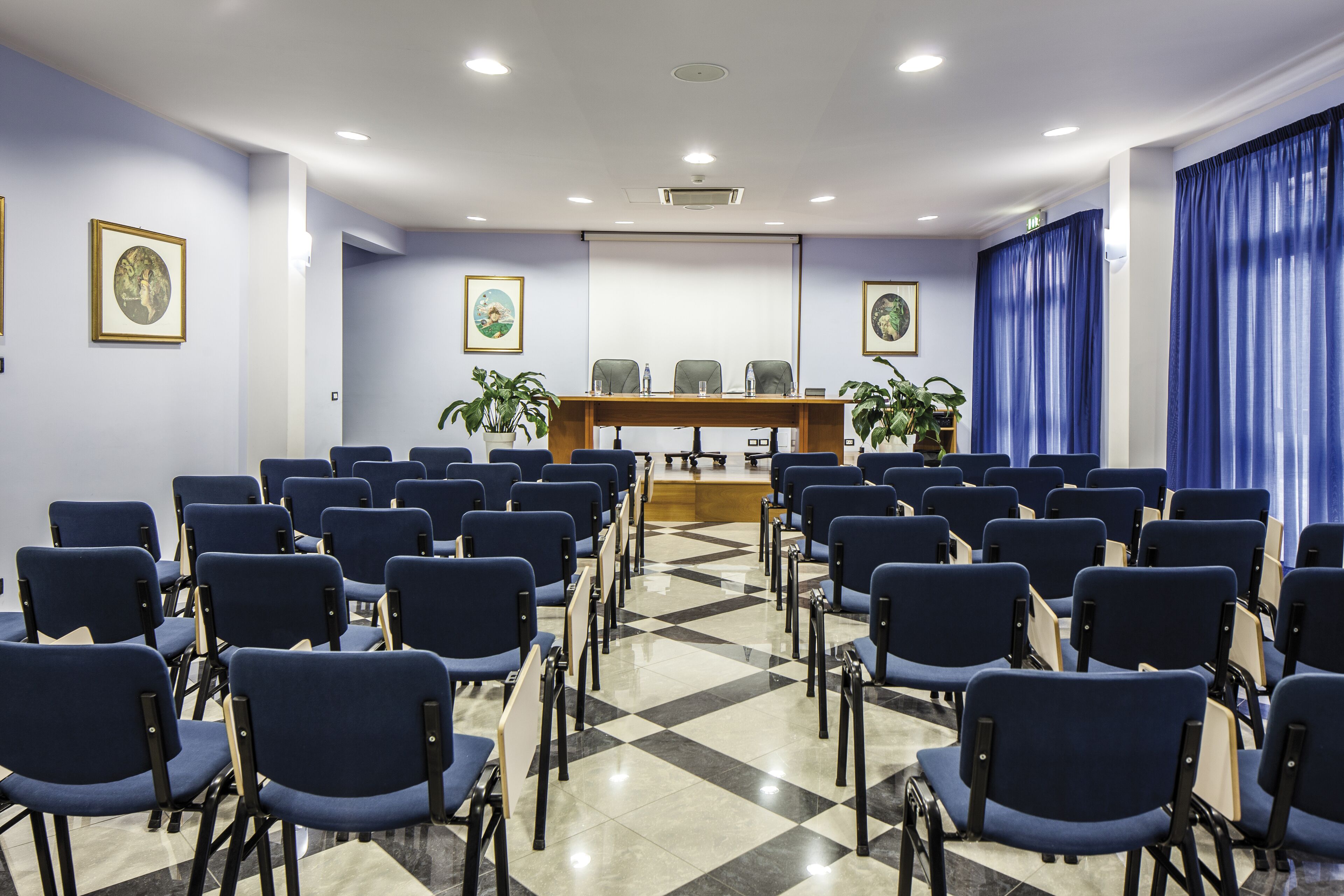 A conference room with rows of chairs, a podium, and framed pictures on the walls.