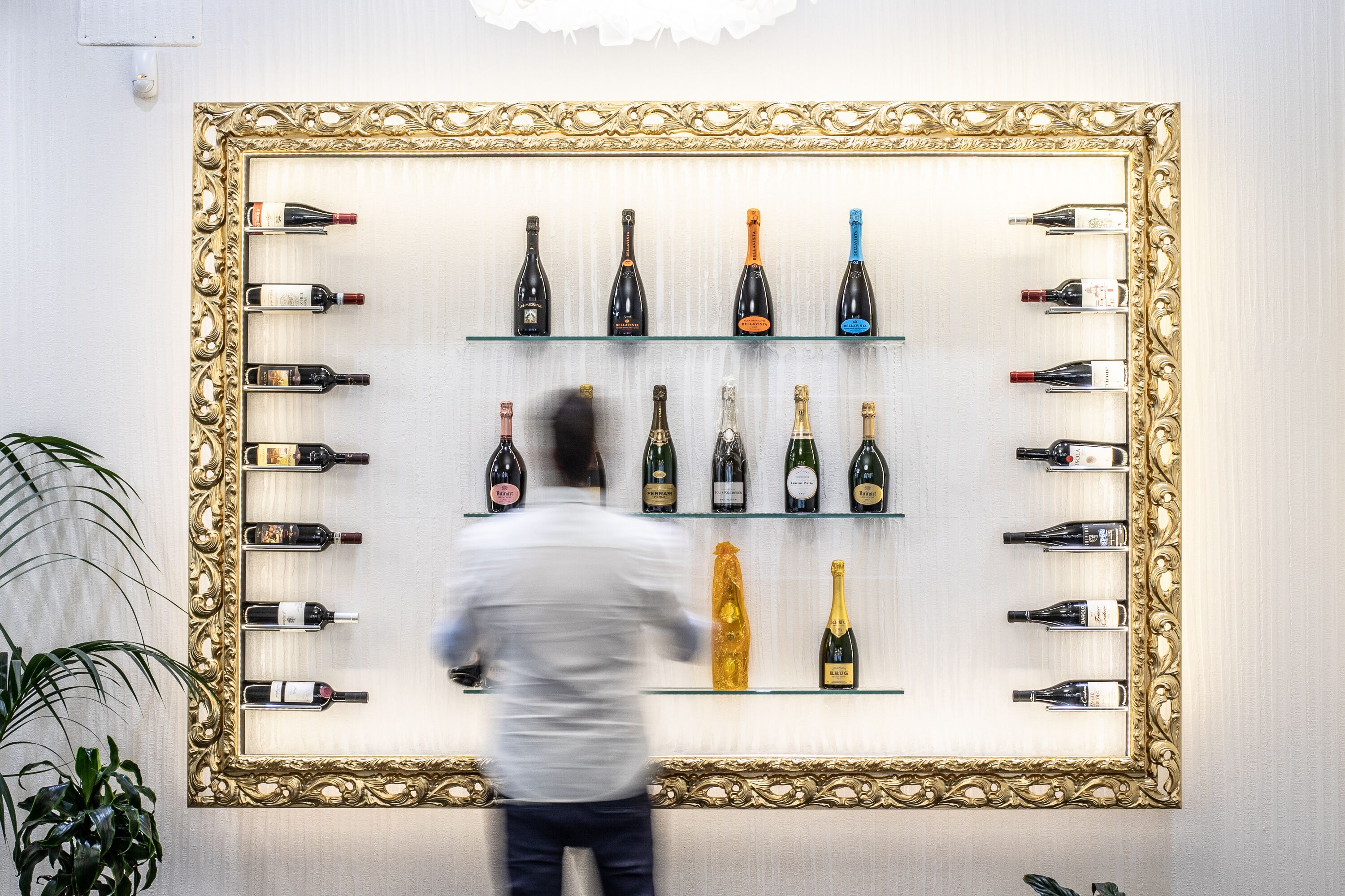 Una parete con un grande specchio decorativo, circondato da scaffali pieni di bottiglie di vino.