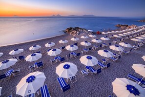 Una playa con hileras de sombrillas y sillas de descanso, dispuestas para tomar el sol.