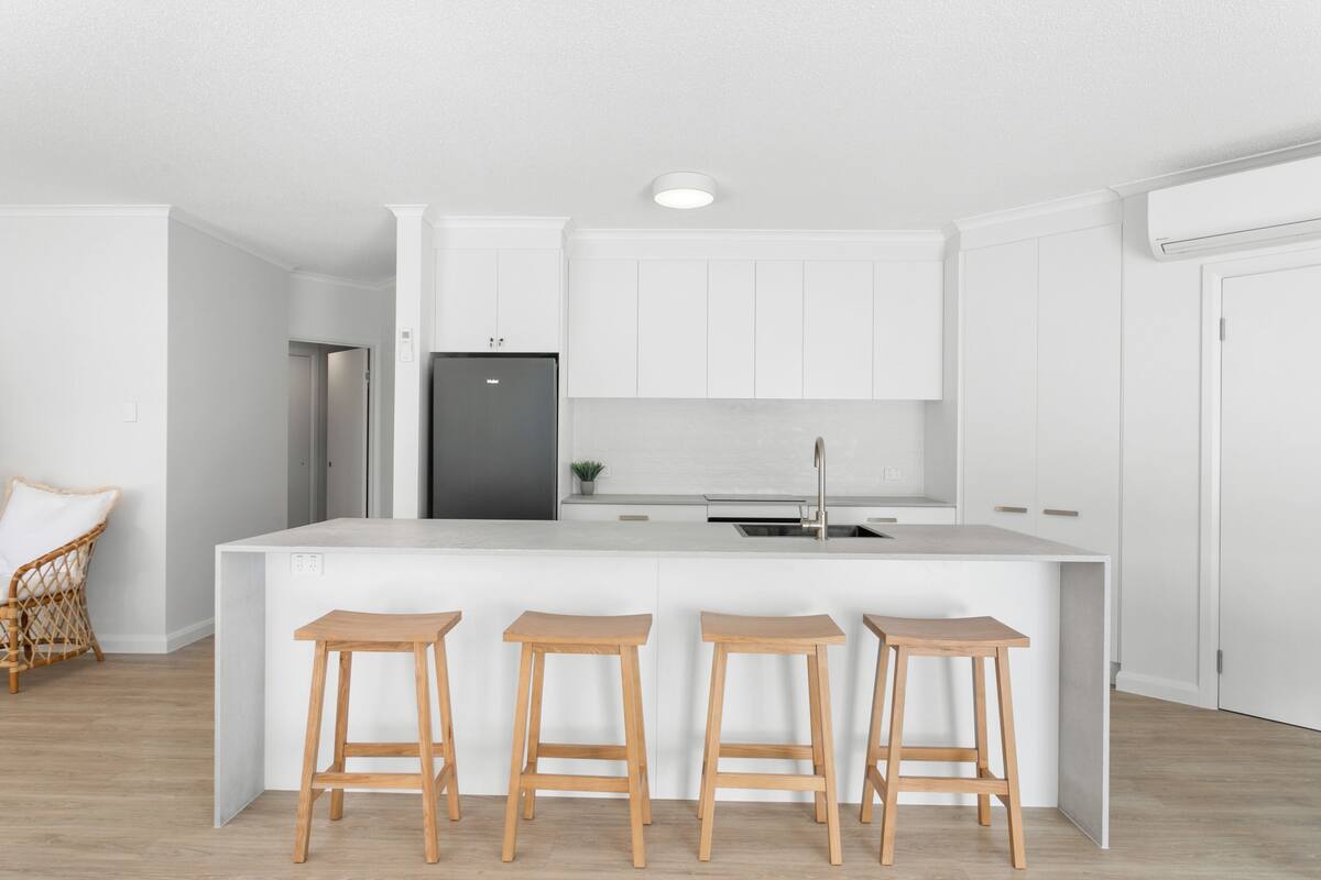Eine moderne Küche mit weißen Schränken, einer zentralen Kochinsel mit Sitzgelegenheiten und einem eingebauten Kühlschrank.