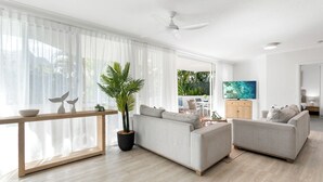 Een moderne woonkamer met een bank, een salontafel en een televisie. Er is een groot raam met dunne gordijnen en een potplant.