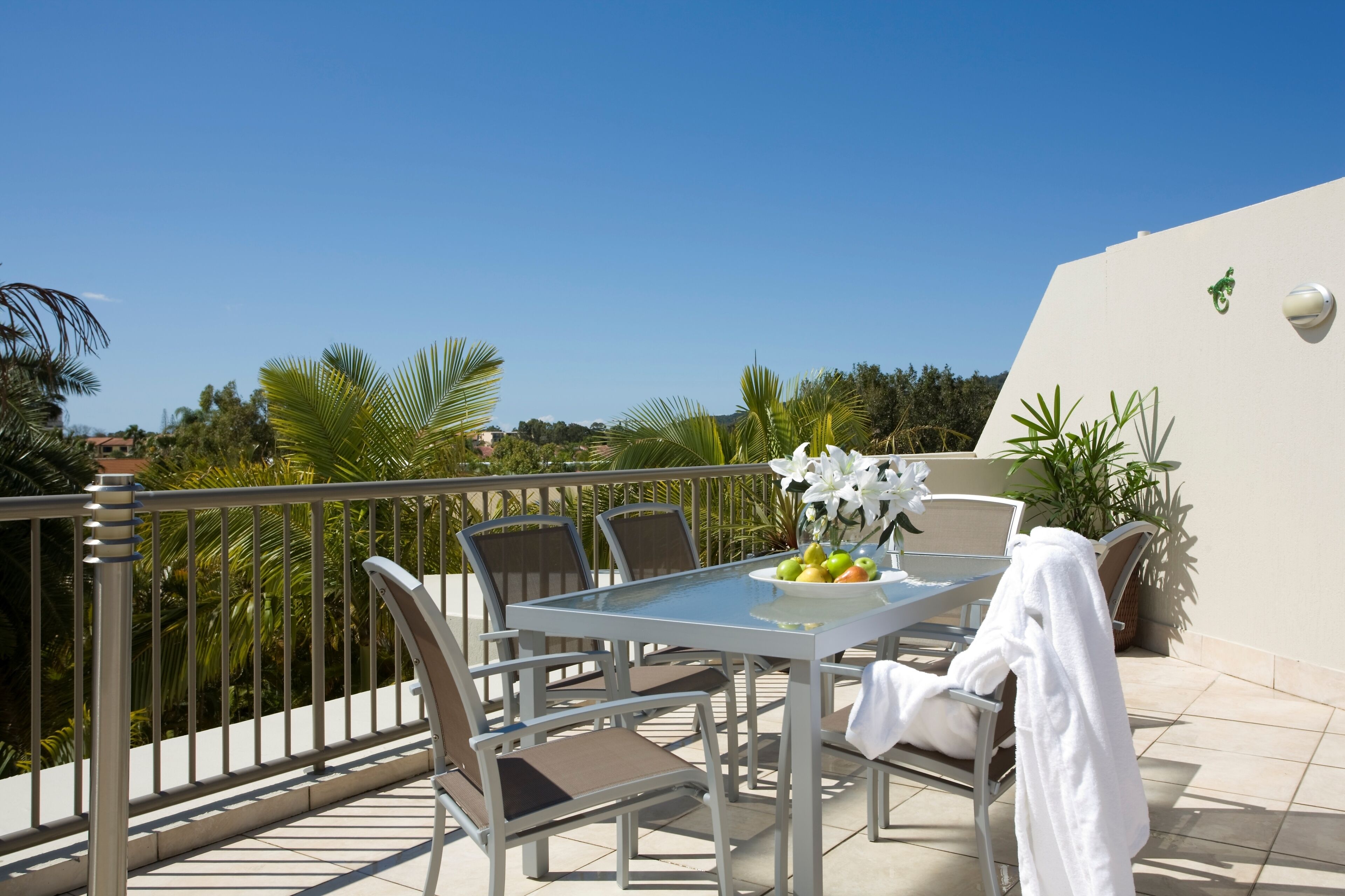 A balcony with a table set for two, chairs, and a potted plant.