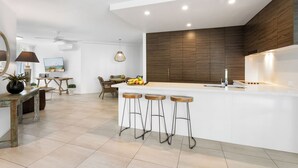 Een moderne keuken met een wit eiland, houten barkrukken en een houten accentmuur.
