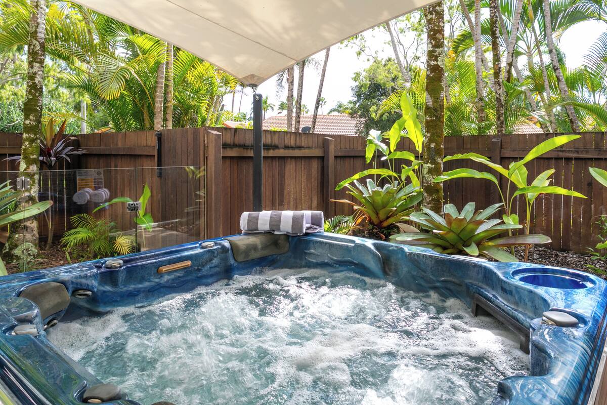 Ein Whirlpool in einem Garten mit Holzzaun, umgeben von verschiedenen Pflanzen und Bäumen.