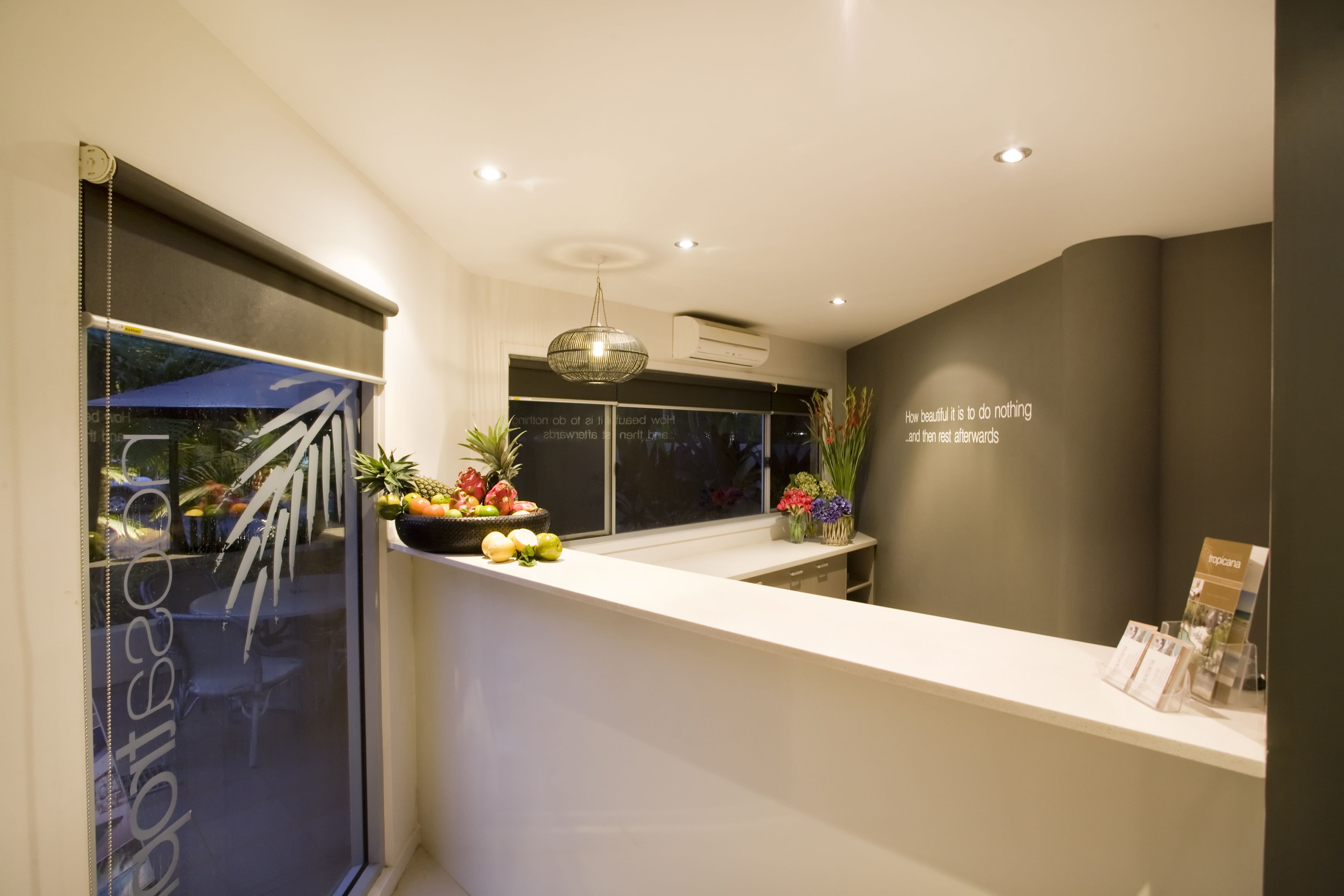 Un espace d’accueil moderne avec un comptoir blanc, un luminaire décoratif suspendu et une fenêtre donnant sur l’extérieur.