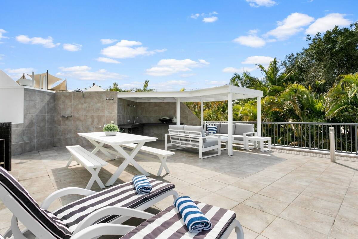 Eine überdachte Terrasse im Freien mit Grill, Sitzgelegenheit und Liegestühlen.