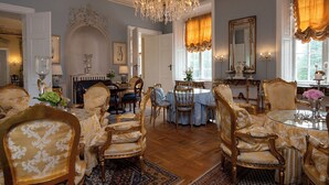 A grand room with ornate furniture, a chandelier, and a classic fireplace.