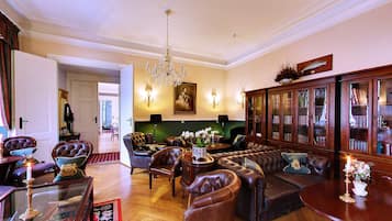 A spacious living room with leather sofas, a chandelier, and a large wooden cabinet with glass doors.