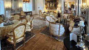 A spacious, elegantly furnished living room with high ceilings, ornate chandeliers, and classic furniture.