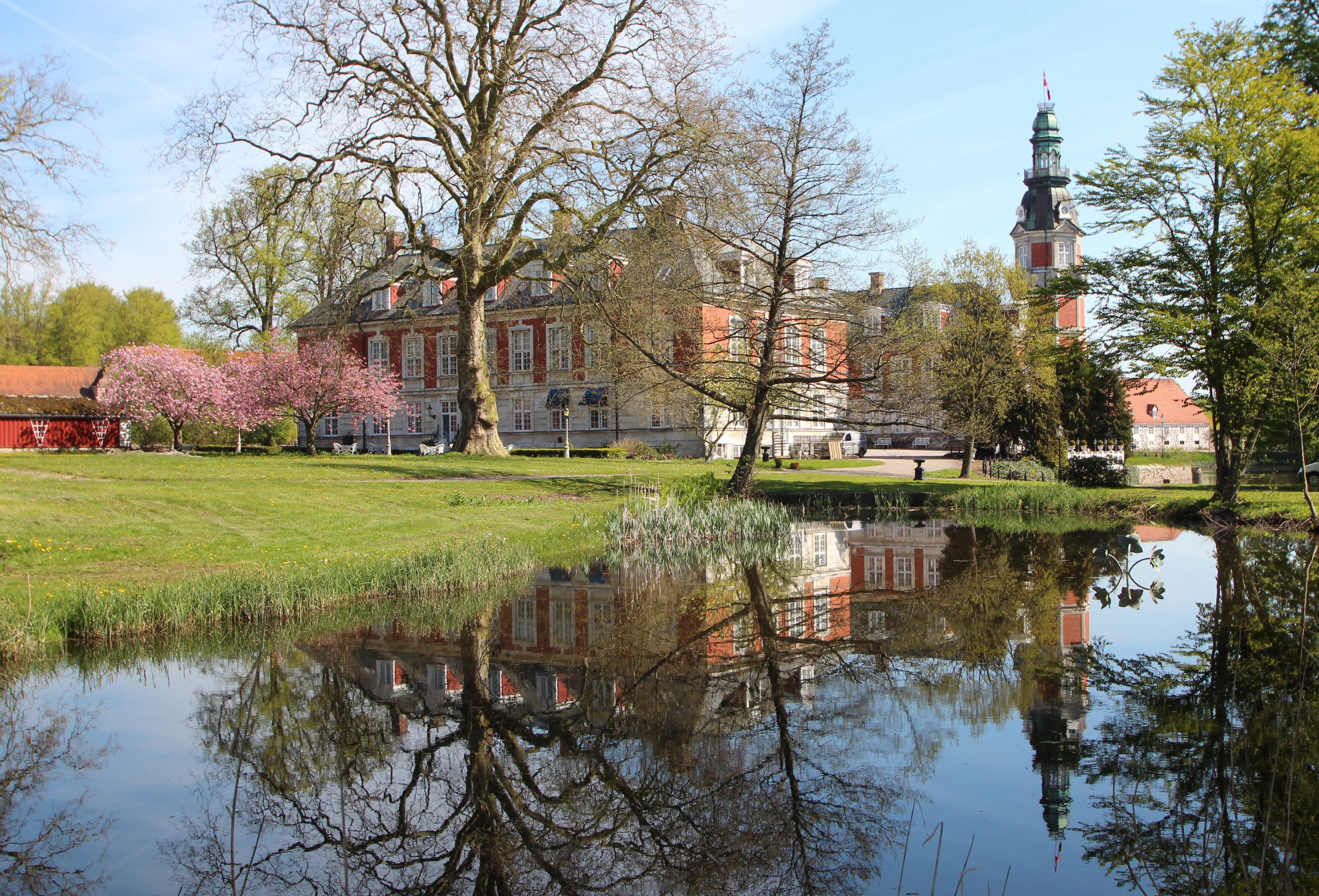 A historic building with a reflection in a pond, surrounded by trees and a clear sky.