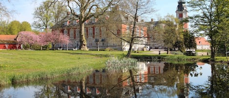 A historic building with a reflection in a pond, surrounded by trees and a clear sky.