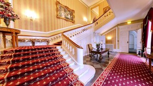 A grand staircase with red carpeted steps, a wooden railing, and a chandelier.