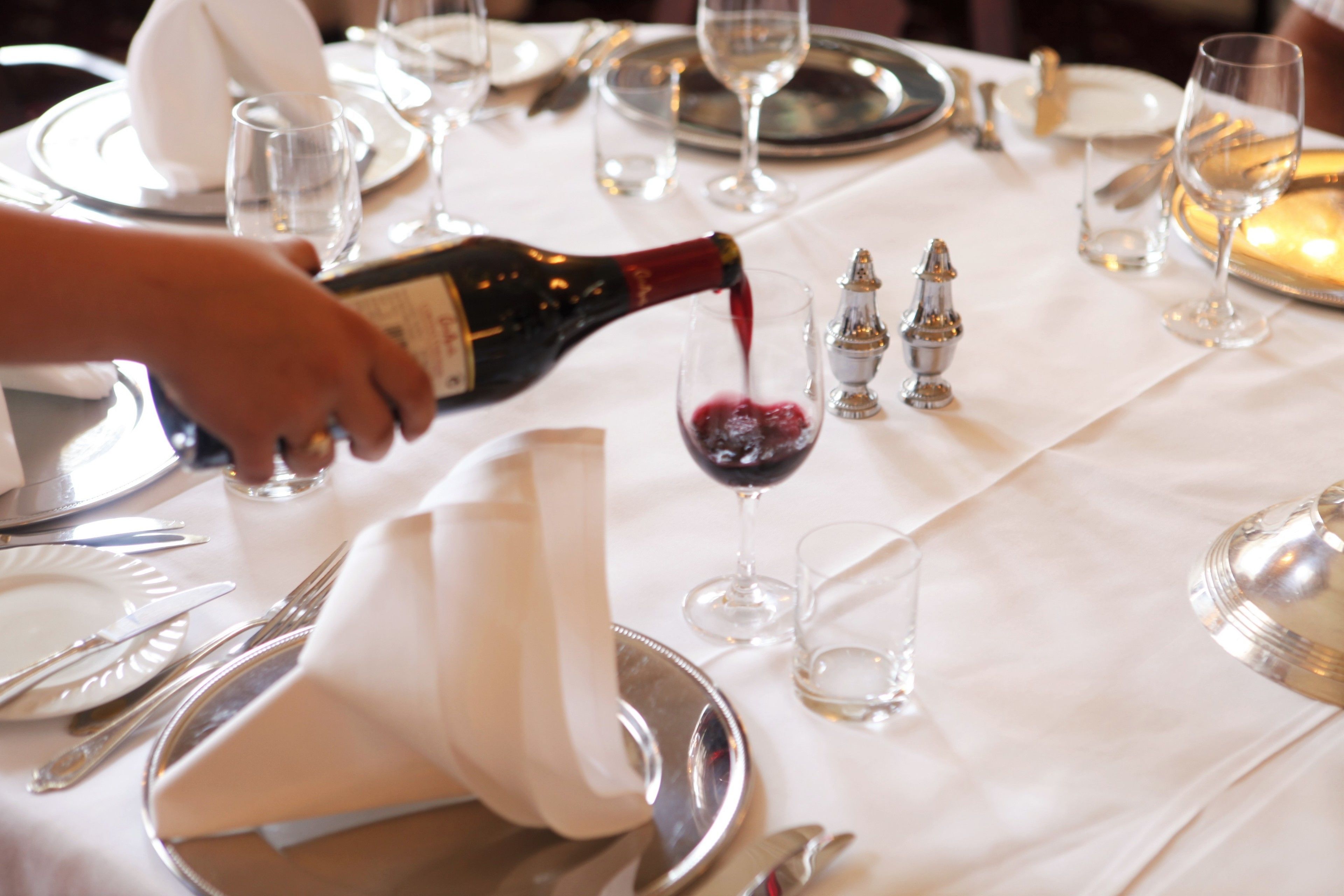 Mesa posta para refeição, com uma garrafa de vinho tinto sendo servida em um copo.