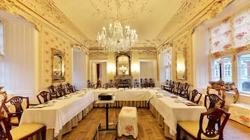 A formal dining room with ornate chandeliers, floral wallpaper, and a long table set for a meal.