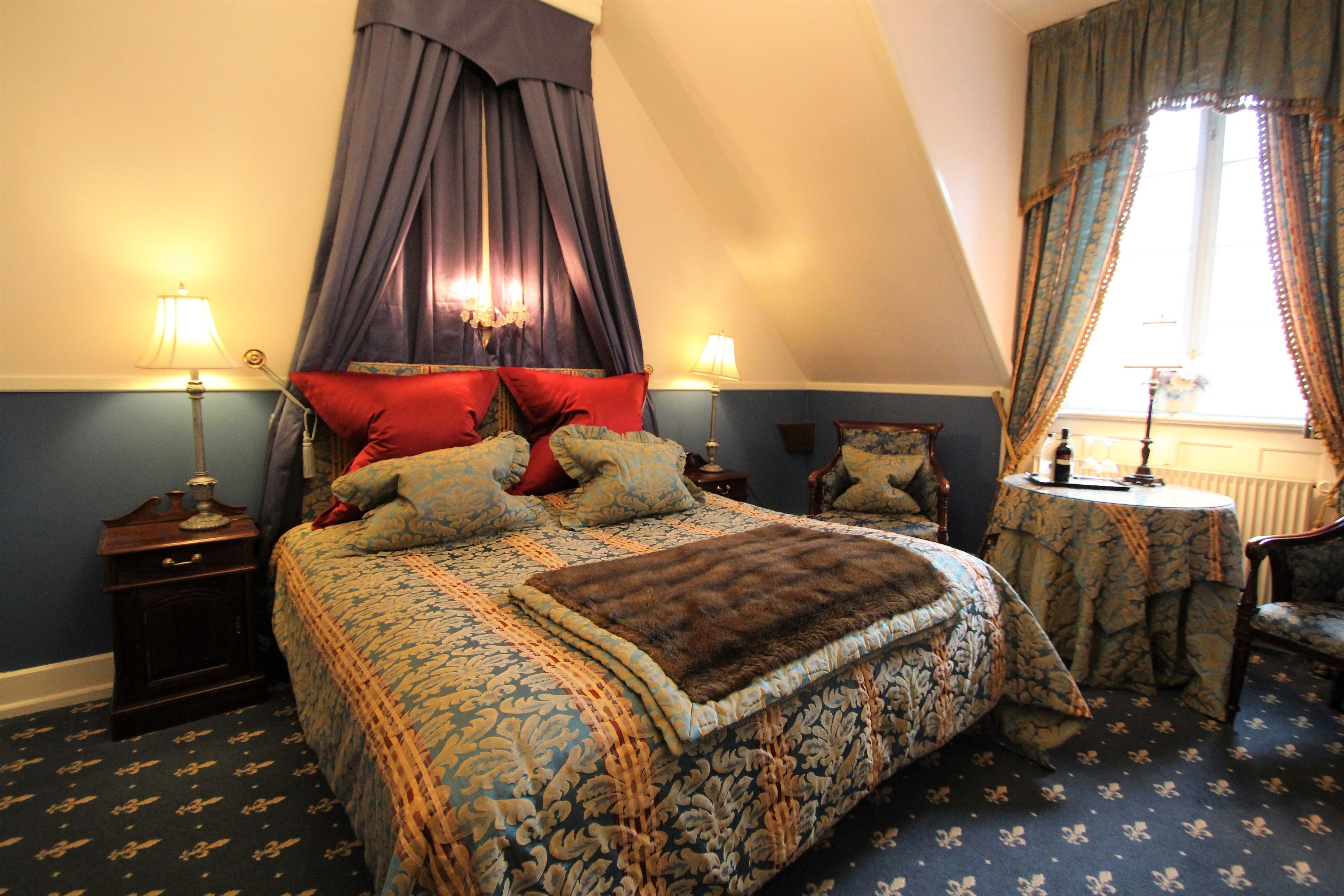 Une chambre avec un grand lit, deux tables de chevet, une chaise, une petite table ronde et une fenêtre avec des rideaux.